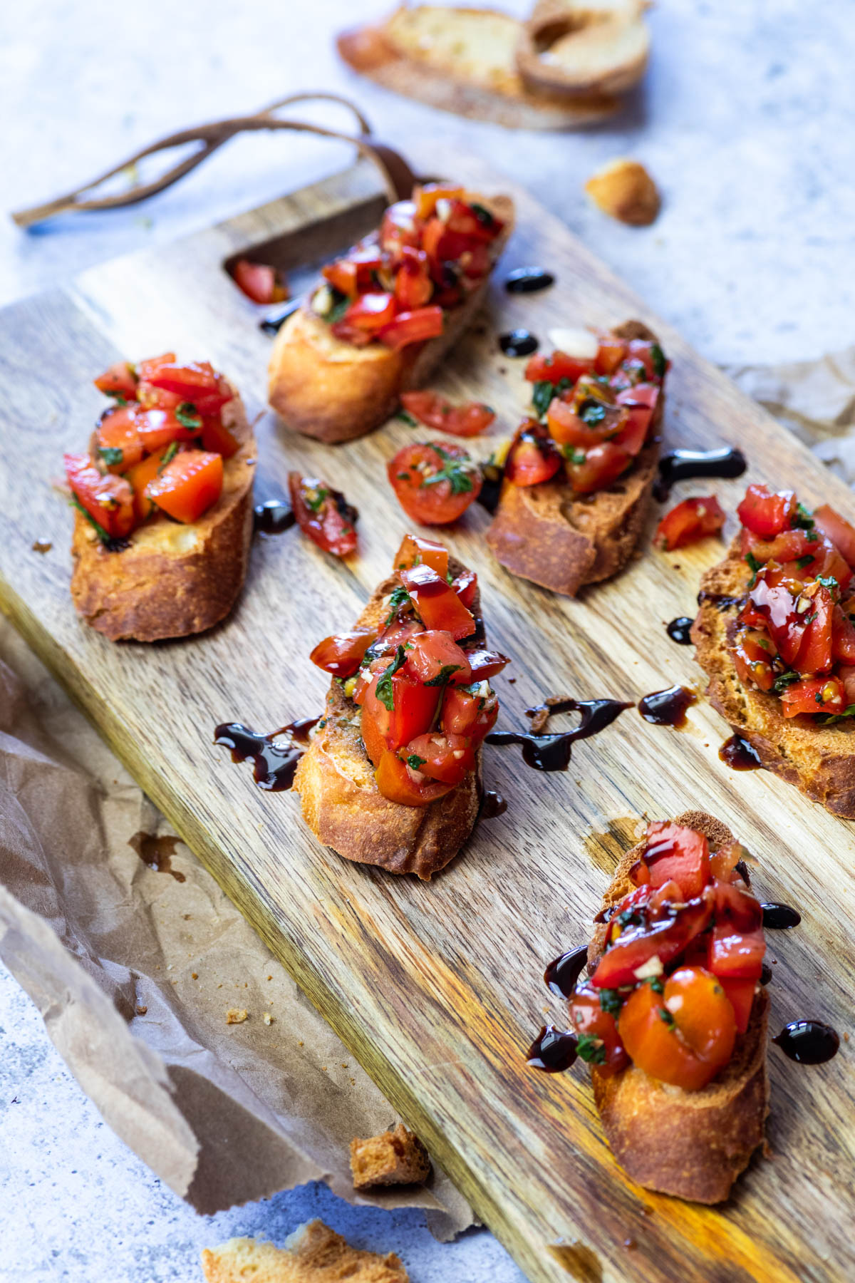 Bruschetta Crostinis served on a wooden board with one crostini in focus.