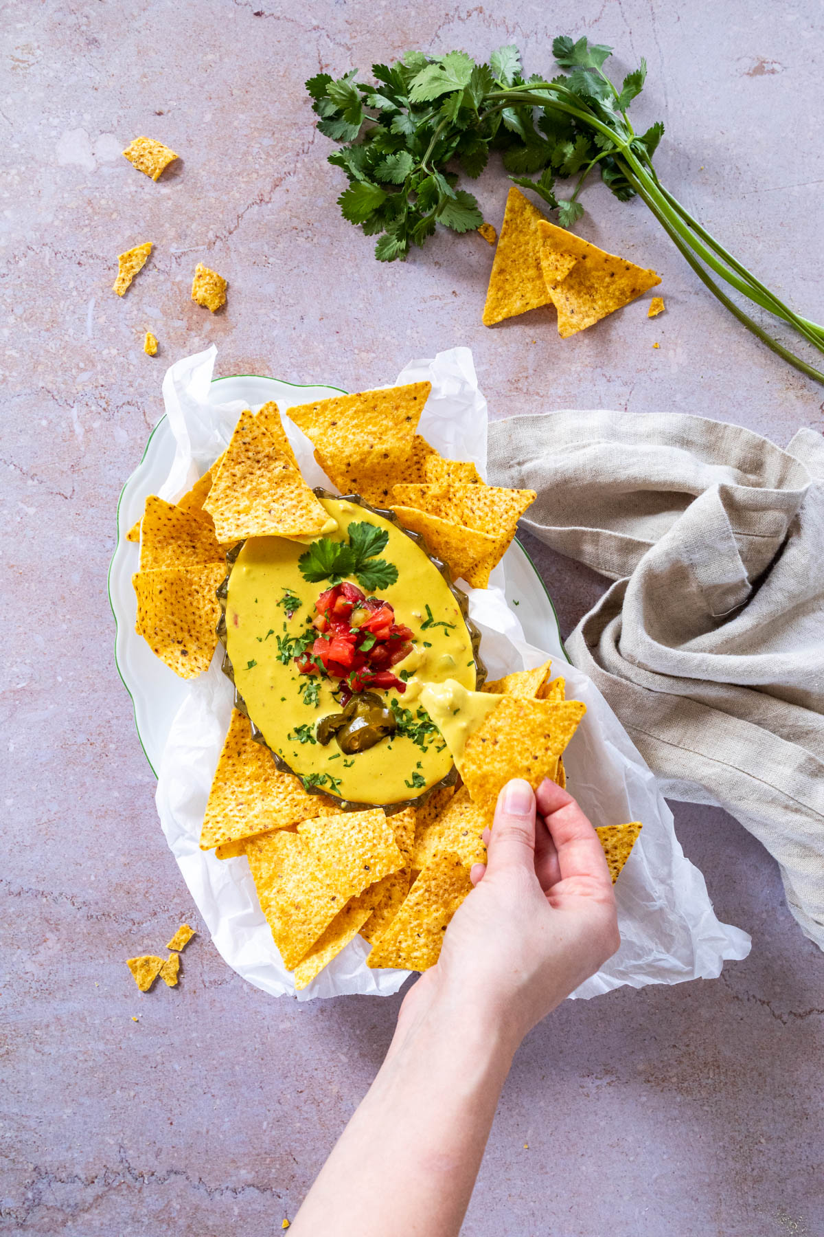 Holding one tortilla chip dipped in vegan queso dip