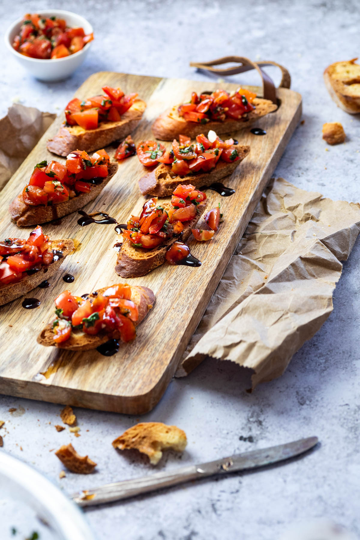 Tomaten-Bruschetta auf Crostinis serviert auf einem Schneidebrett mit Balsamico Creme