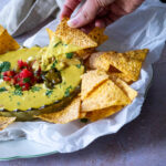 einen Chip halten und in den veganen Queso-Dip tauchen