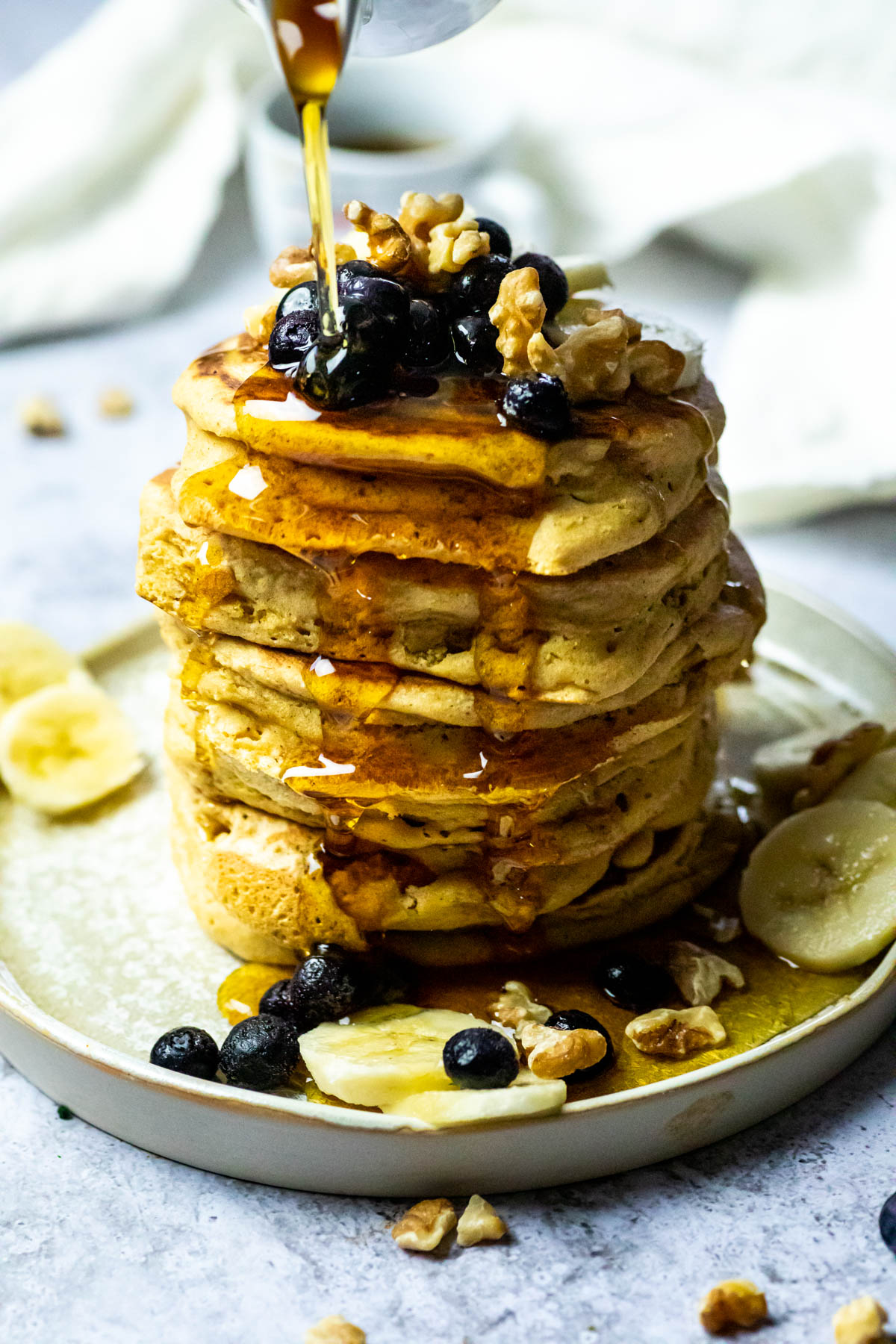 Close up of a stack of vegan pancakes and pouring some maple syrup over.