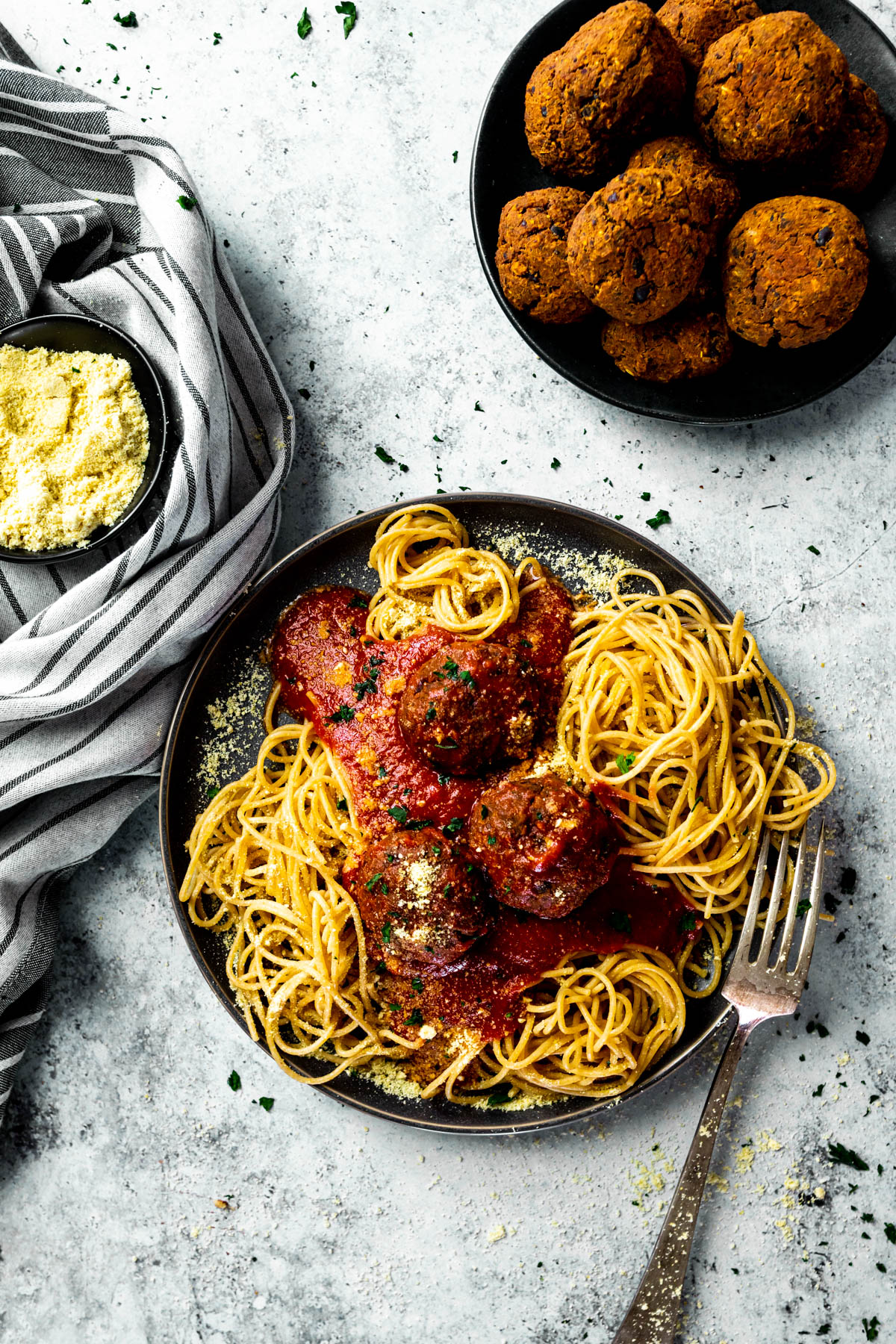 Vogelblick auf einen Teller mit Spaghetti, veganen Fleischbällchen und Marinara-Sauce und einen Teller mit Fleischbällchen und eine Schüssel mit veganem Parmesan.