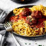 In focus vegan meatballs served on top of spaghetti and marinara sauce on a plate.