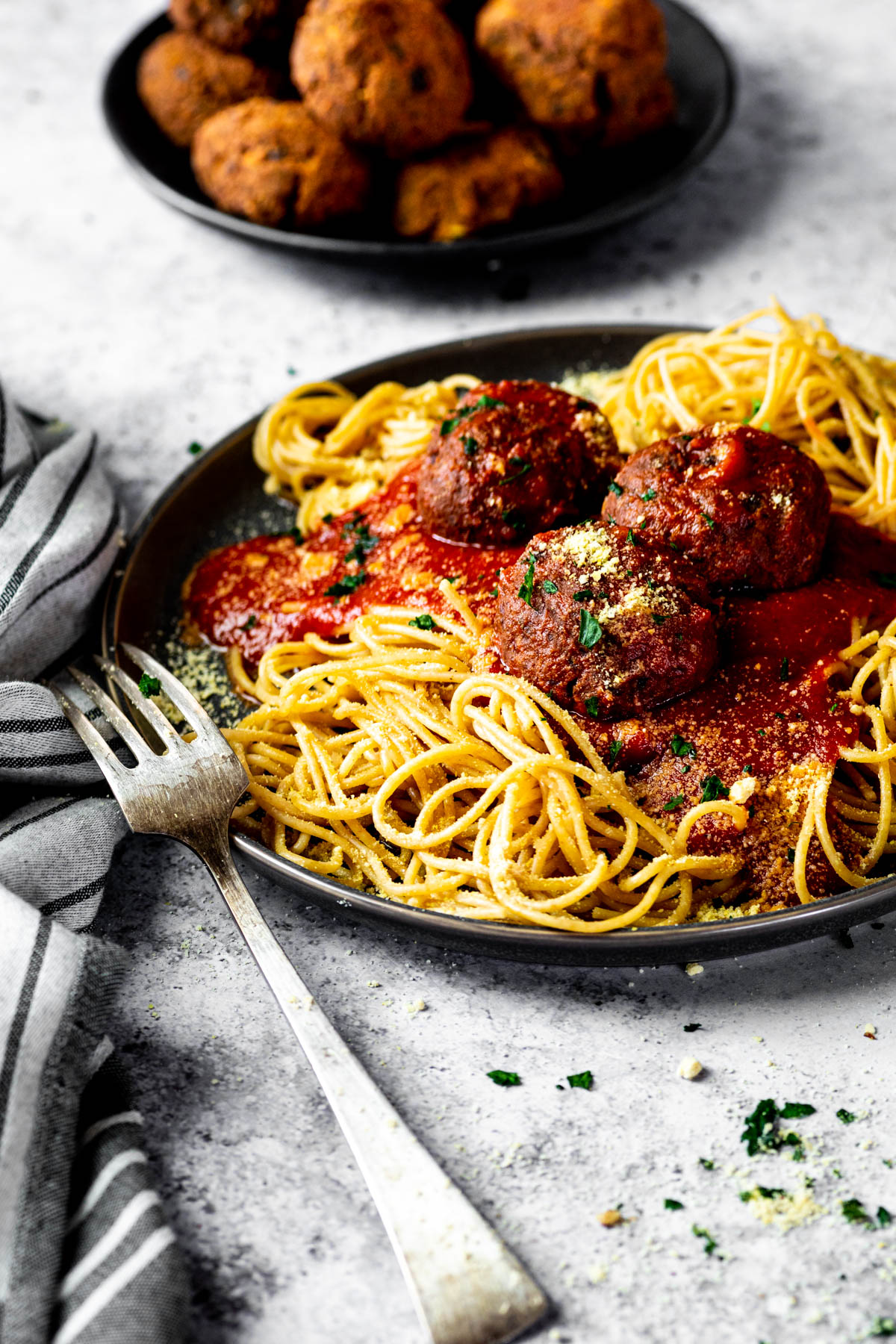 In focus vegan meatballs served on top of spaghetti and marinara sauce on a plate.