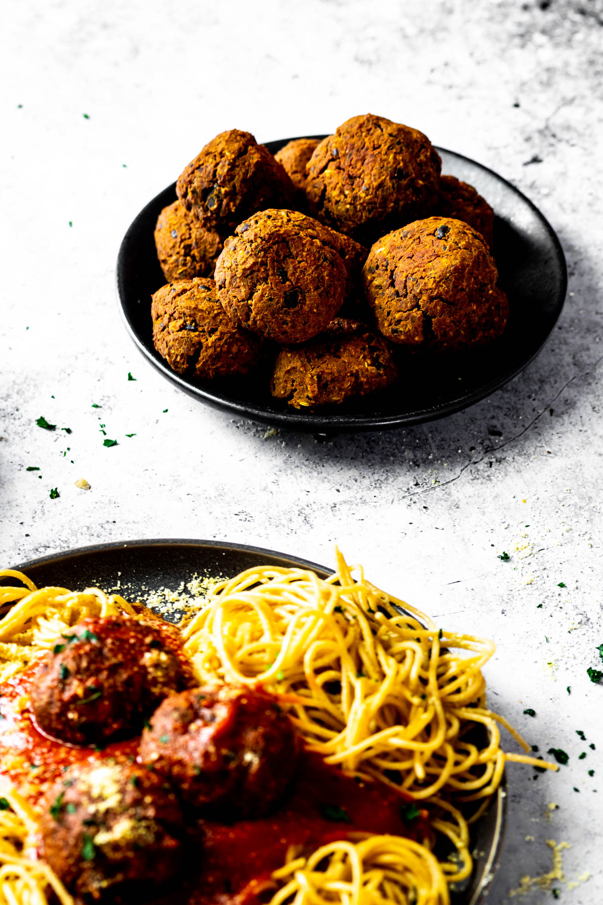 Kleiner Teller mit ein paar veganen Fleischbällchen. Und vorne verschwamm ein Teller mit Spaghetti und veganen Fleischbällchen