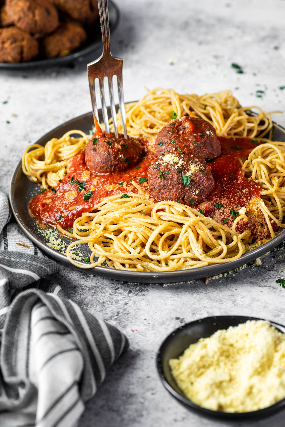 Die Gabel steckt in einem veganen Fleischbällchen, das mit Spaghetti und Marinara-Sauce auf einem Teller serviert wird.