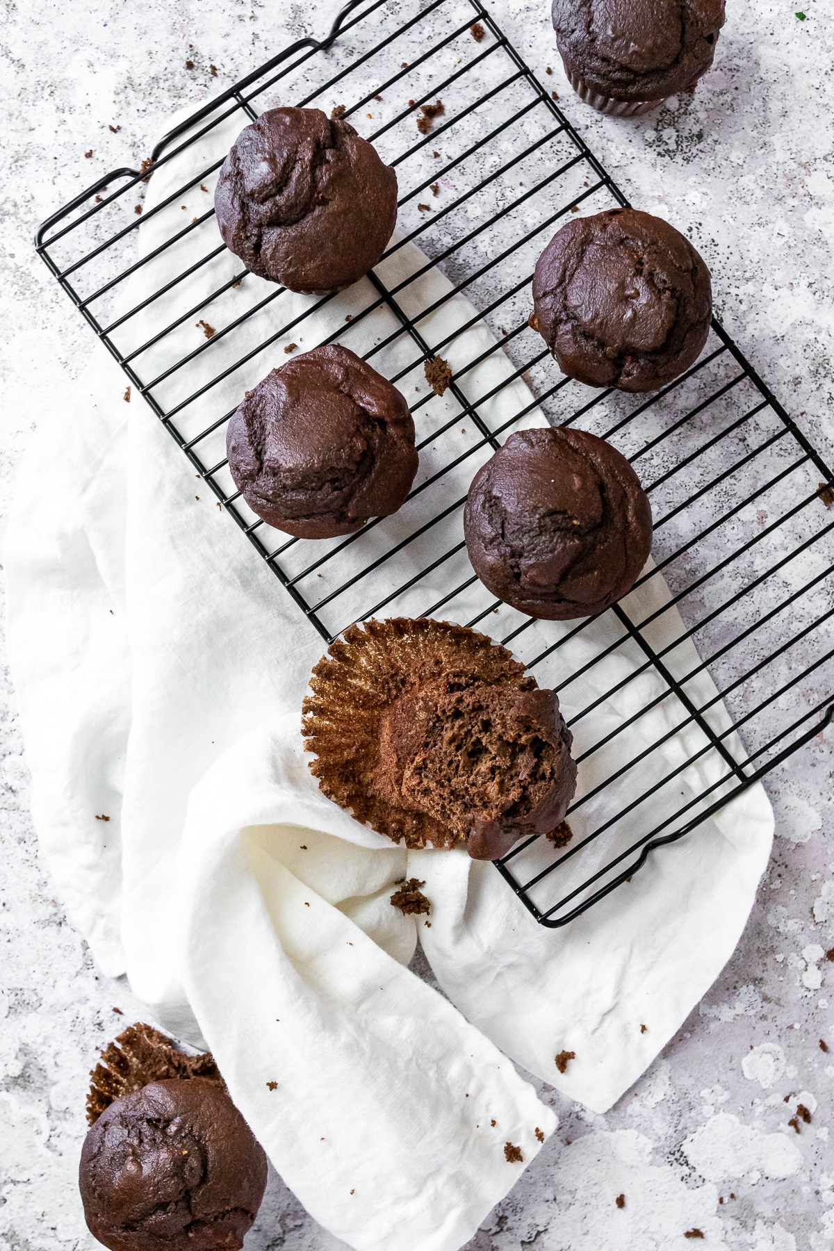 Bird view of 7 chocolate muffins on a wire rack with a cloth on the side.