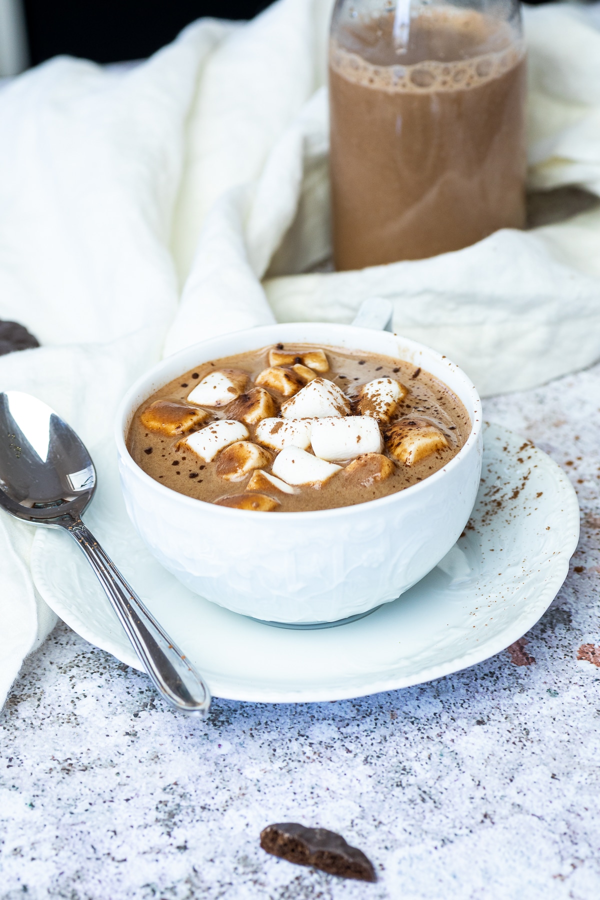 Vegane heiße Schokolade in einer Tasse mit einer Flasche mit Schokoladenmilch im Hintergrund.