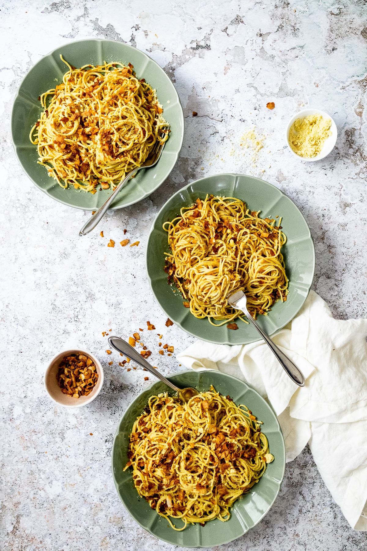 Bird view of 3 bowls with spaghetti carbonara and a dipping bowl with coconut bacon and vegan parmesan.