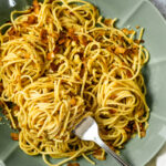 A fork full with spaghetti carbonara is laying in a bowl with spaghetti carbonara.
