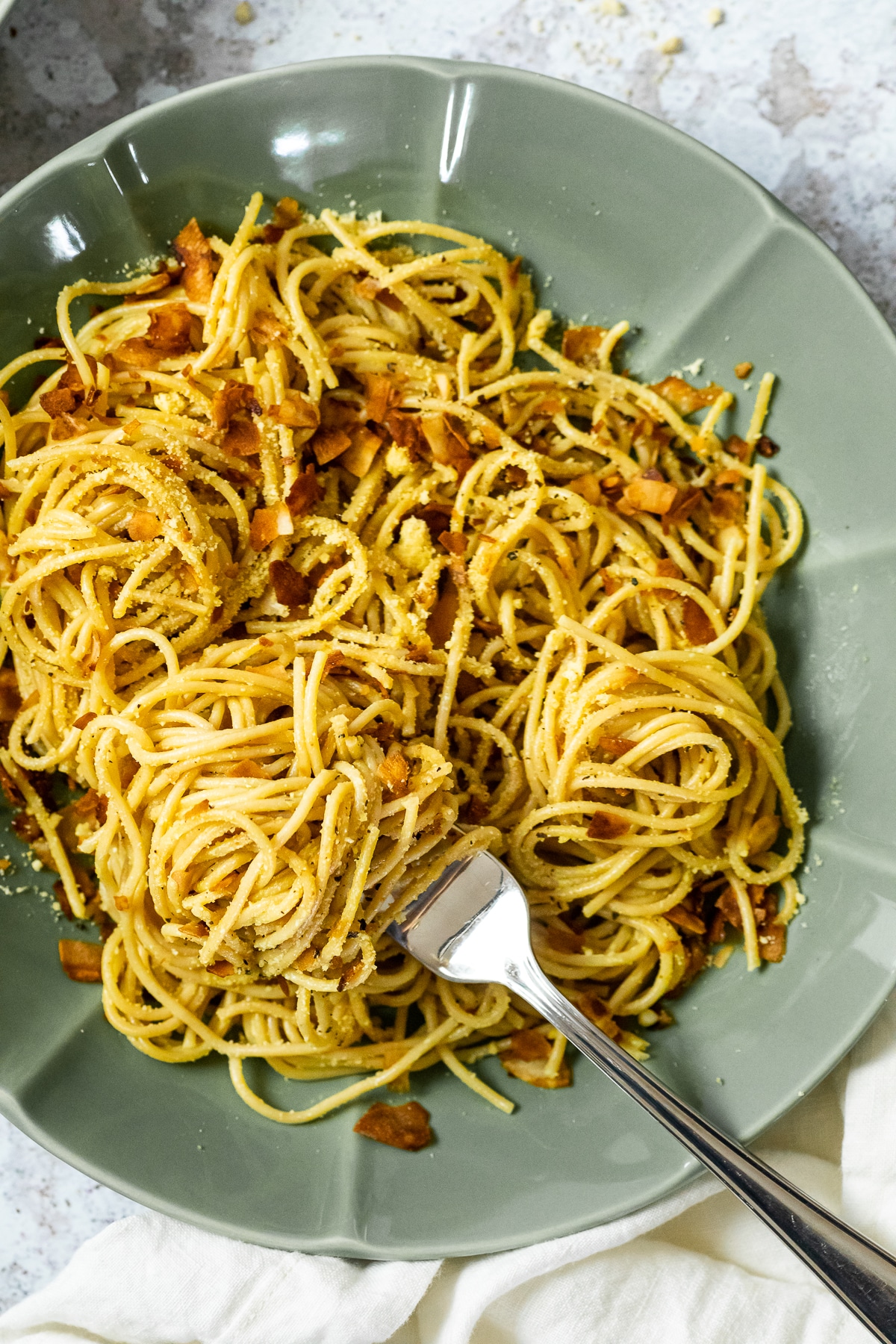 A fork full with spaghetti carbonara is laying in a bowl with spaghetti carbonara.