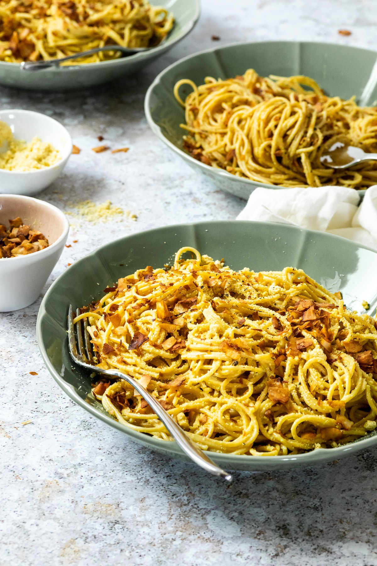 3 plates of spaghetti carbonara with one in focus.