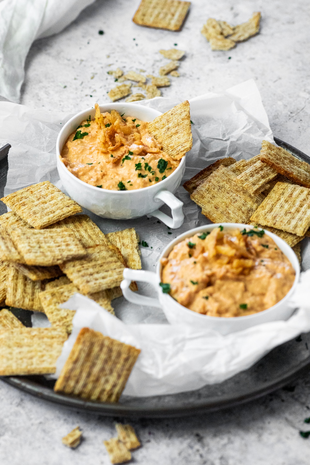 Zwei Tassen mit veganem Zwiebel-Knoblauch-Dip, serviert auf einer Platte mit Cracker.