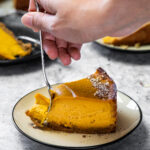 Taking some pumpkin cheesecake with a fork from a piece on a plate.