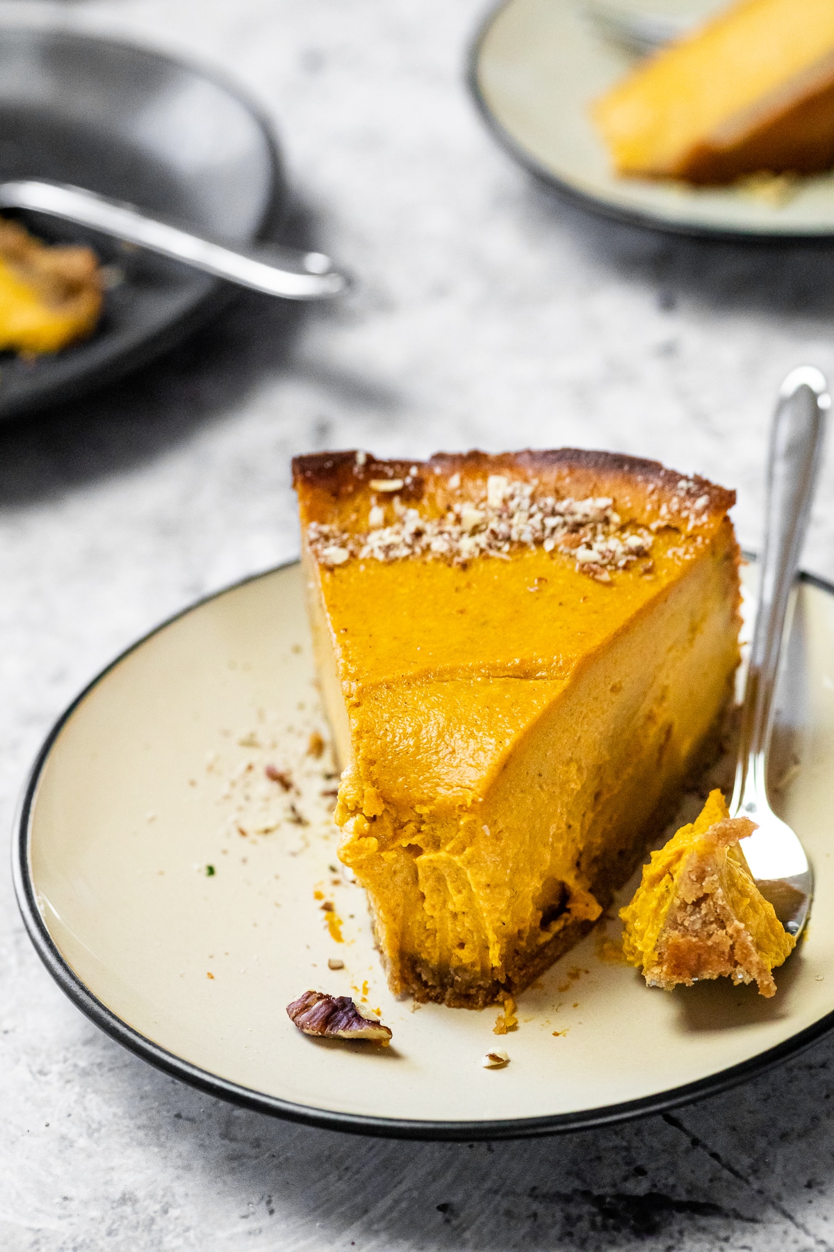 A piece of pumpkin cheesecake served on a plate with a fork which has some cheesecake on it.