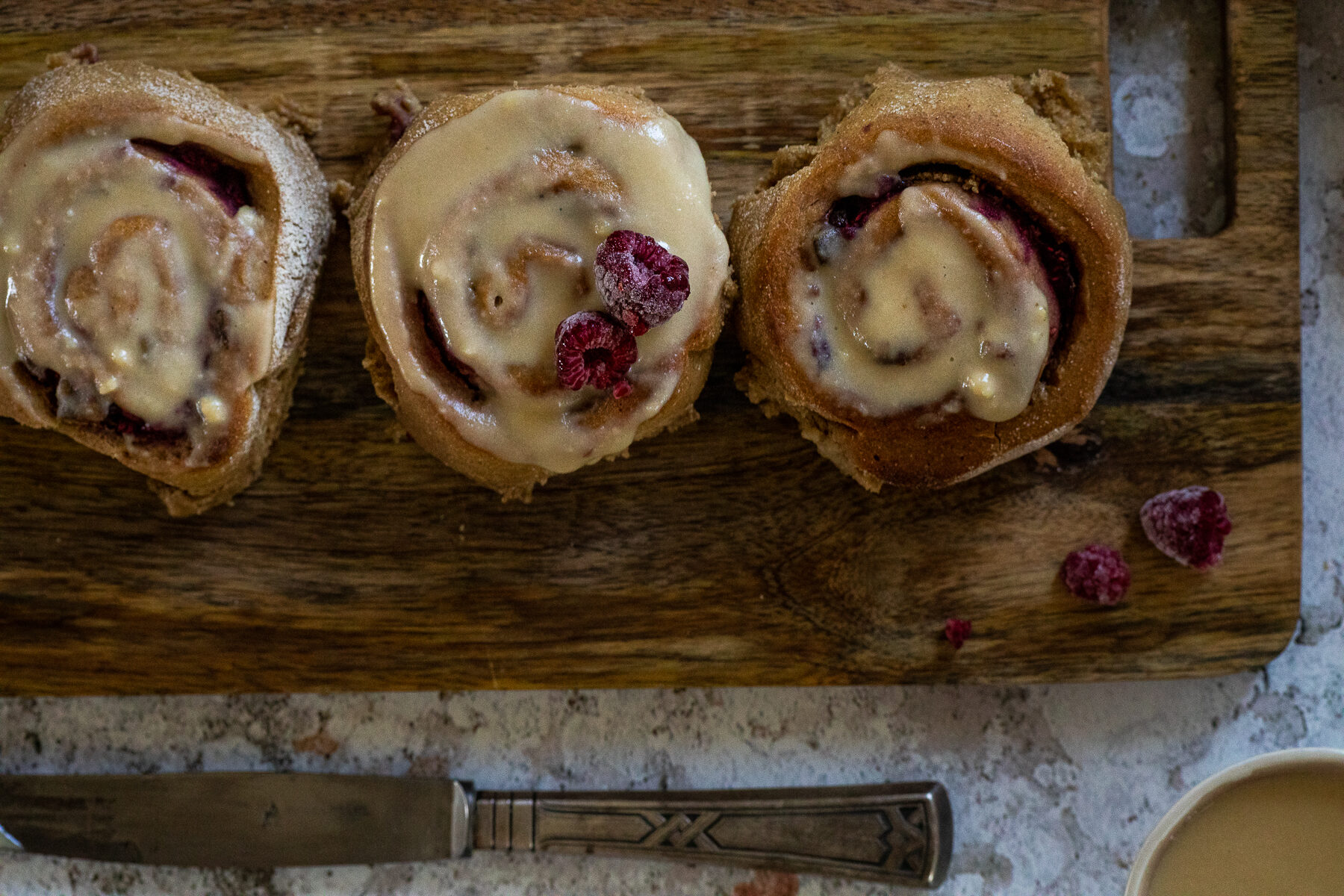 Bird View: 3 vegan raspberry cinnamon buns with an oil free frosting on a wood board.