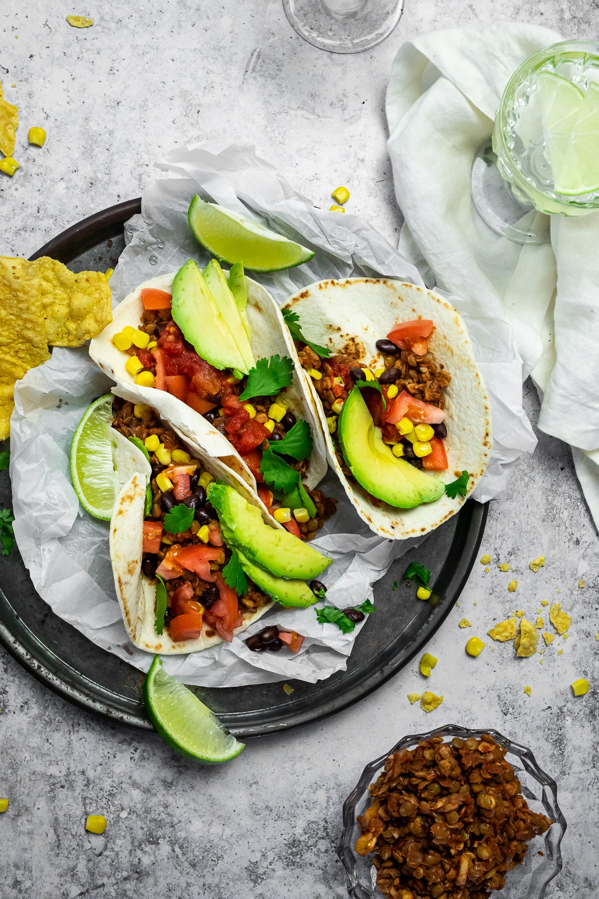 Bird view of 3 tacos on a serving plate with a bowl of vegan taco meat and a cup with water.