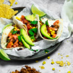 Servierteller mit Pergamentpapier und 3 Tacos darüber und serviert mit Tortillachips
