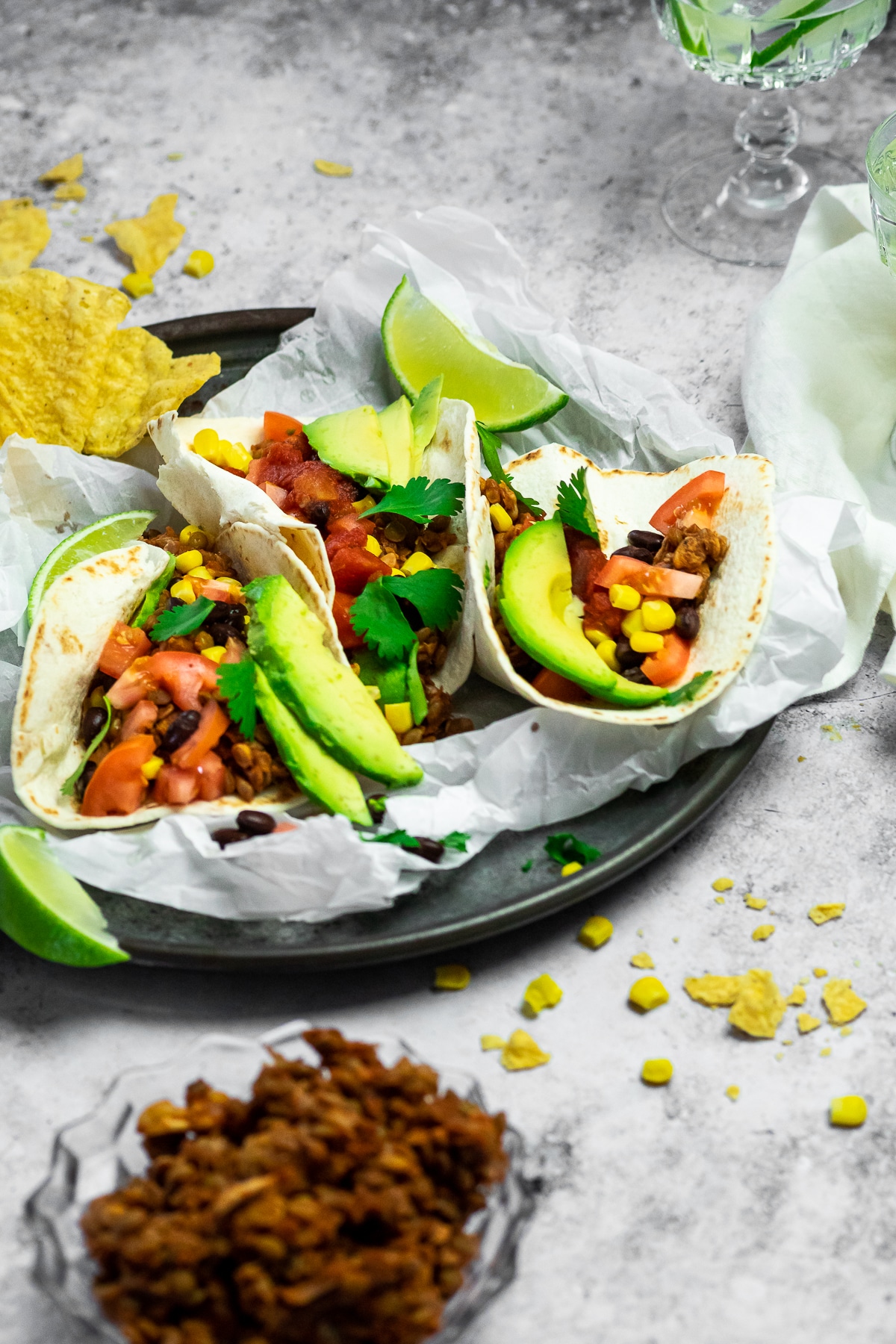 Serving plate with parchment paper and 3 Tacos on top and served with tortilla chips