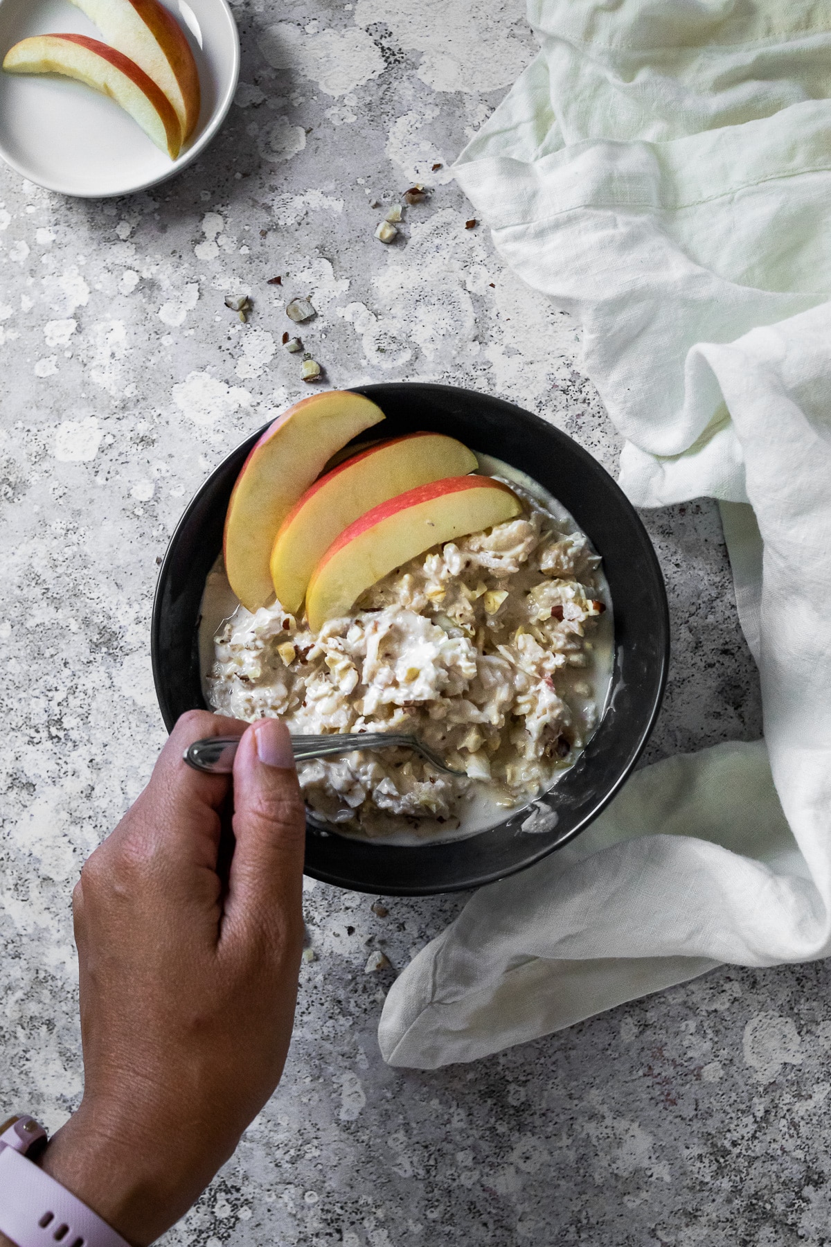 vegan Bircher Muesli in a dark bowl with holding a spoon in that bowl.