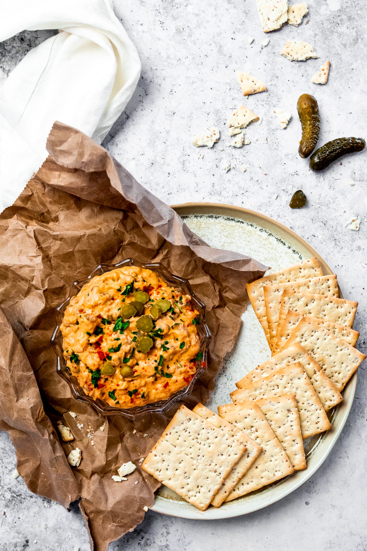 Vogelansicht eines Tellers mit einer Schüssel des veganen Cheeseburger-Dips und der Cracker auf dem Teller. Einige Gurken und Cracker bröckeln zur Dekoration um den Teller