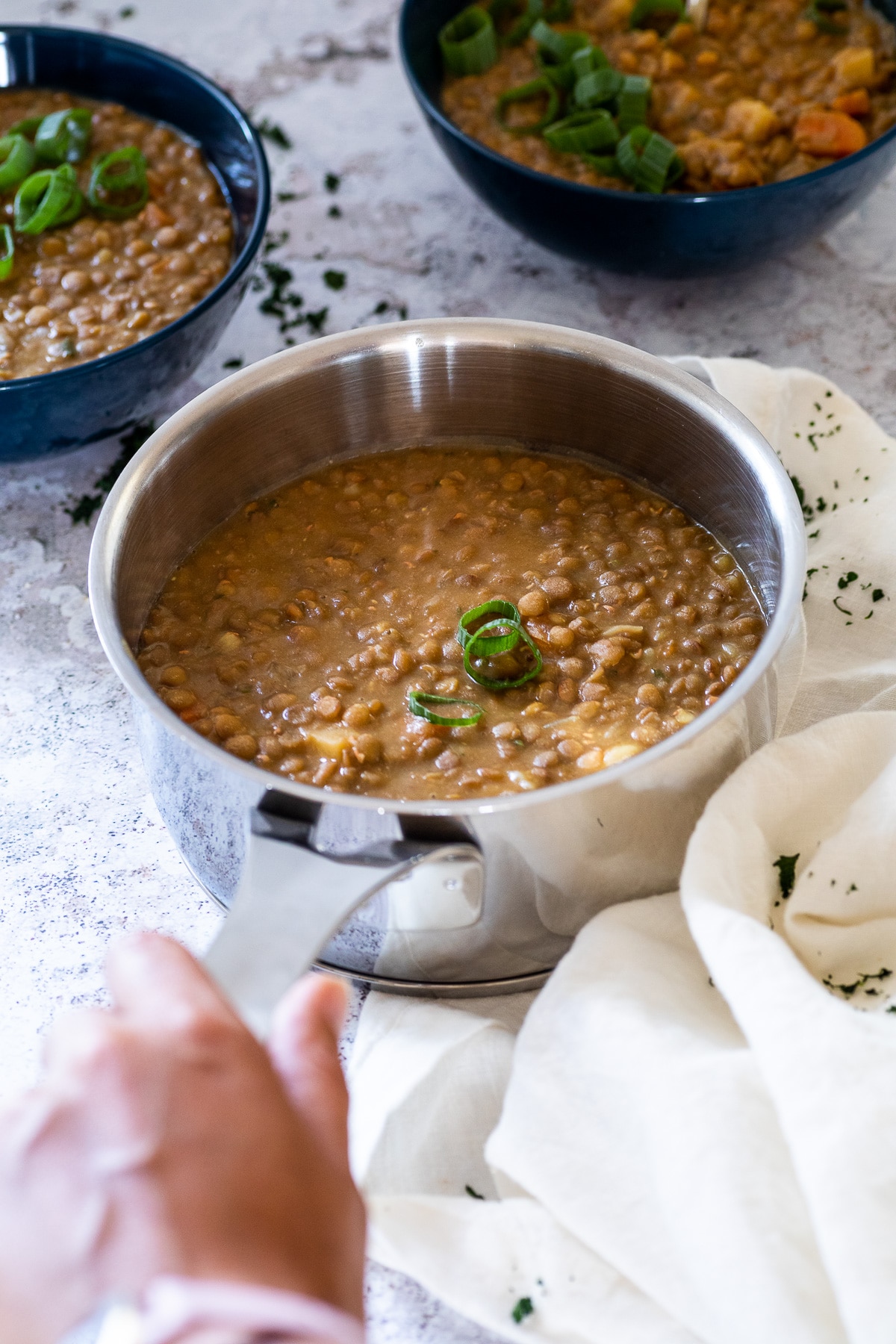 ein Topf mit veganer Linsensuppe wird festgehalten