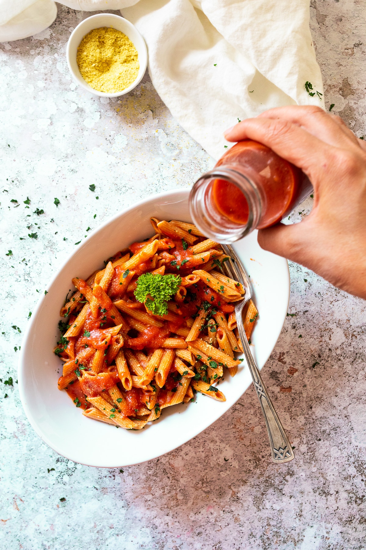 Bird view of a bowl with penne alla vodka and starting to pour some more sauce over it.