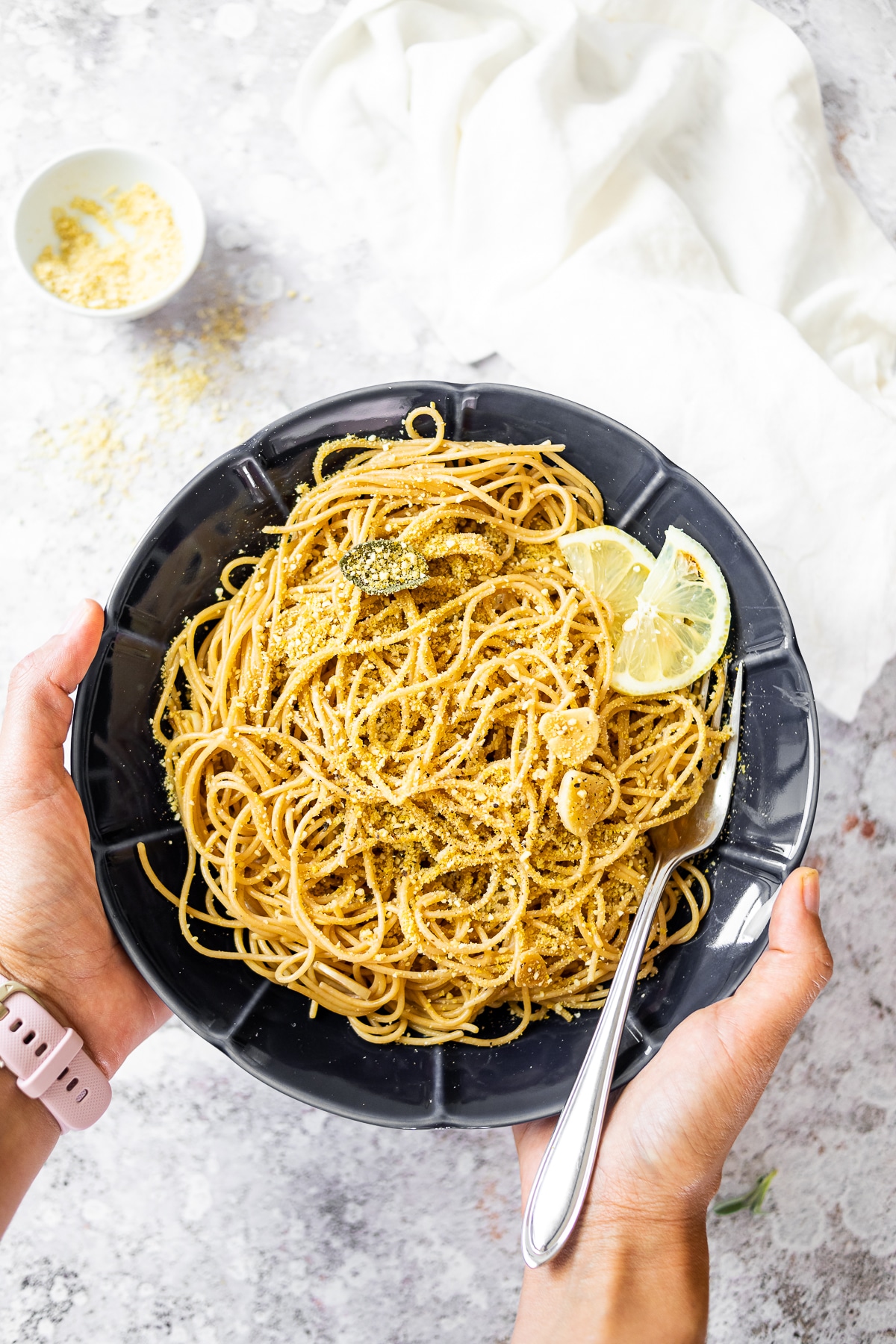 Holding a dark bowl with spaghetti in sage sauce