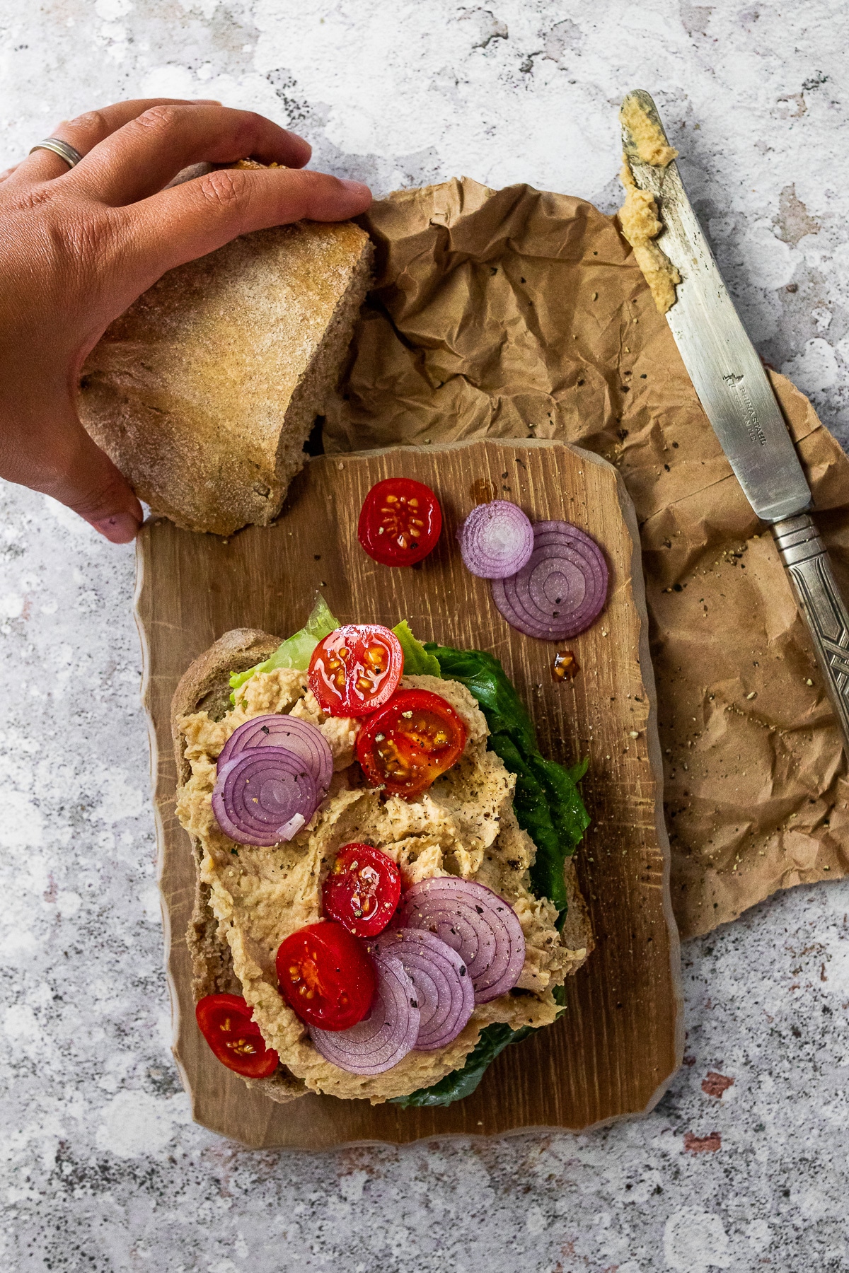 Vogelansicht eines offenen veganen Thunfischsandwiches, das auf einem Holzbrett liegt. Mit einem Messer an der Seite und einem Brötchen zur Hälfte darüber.