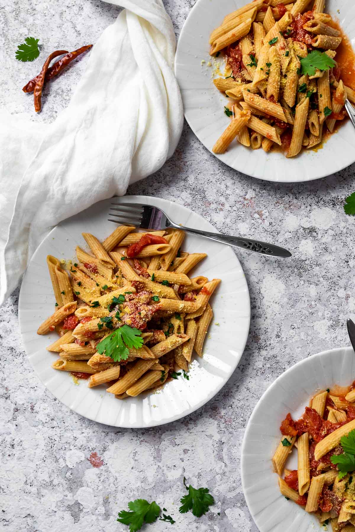 Drei Teller mit Penne alle Arrabiata beladen.