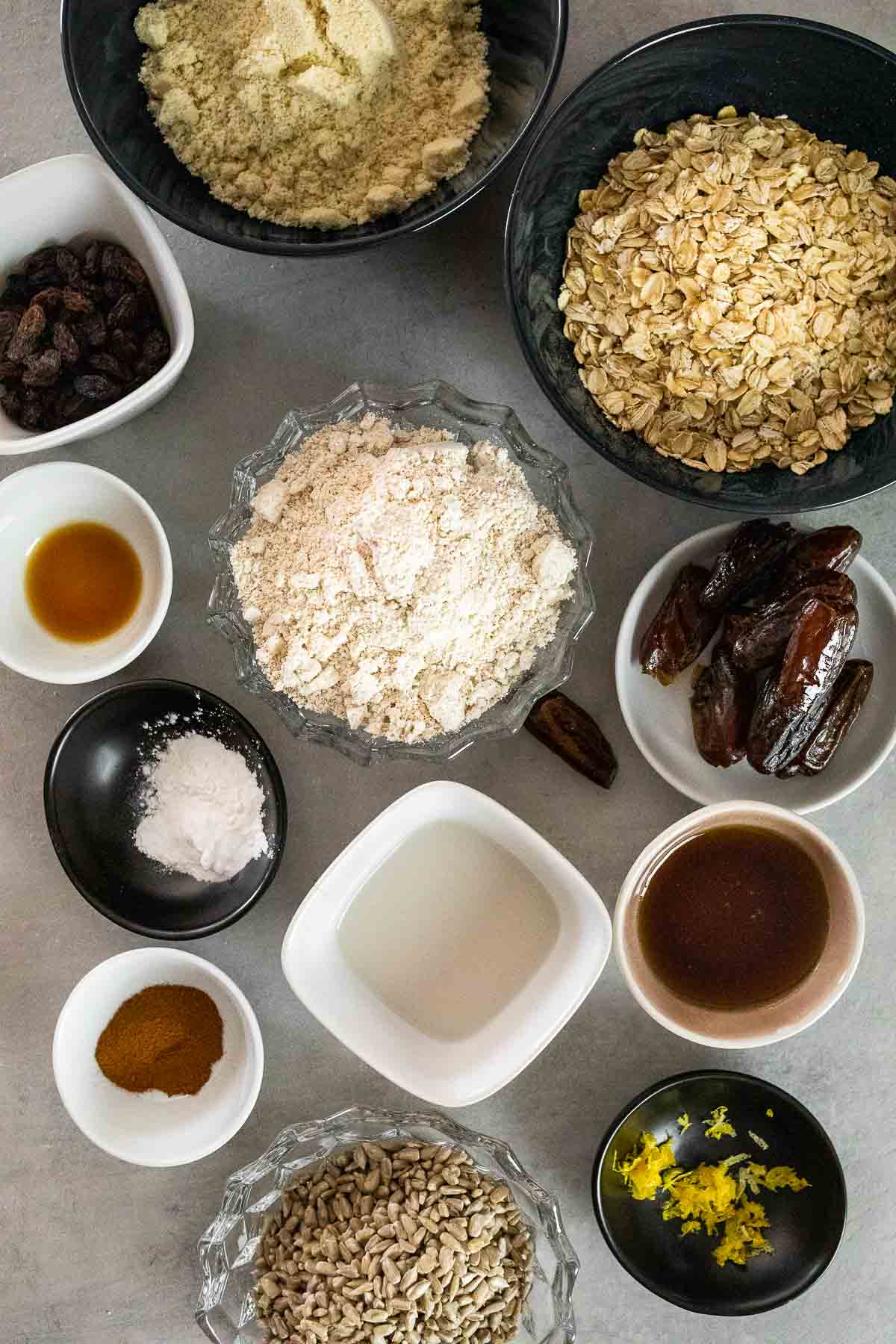 Ingredients of vegan oat cookies, rolled oats, almond flour, oat flour, raisins, dates, vanilla extract, baking powder, cinnamon, sunflower seeds, lemon zest, almond milk, maple syrup