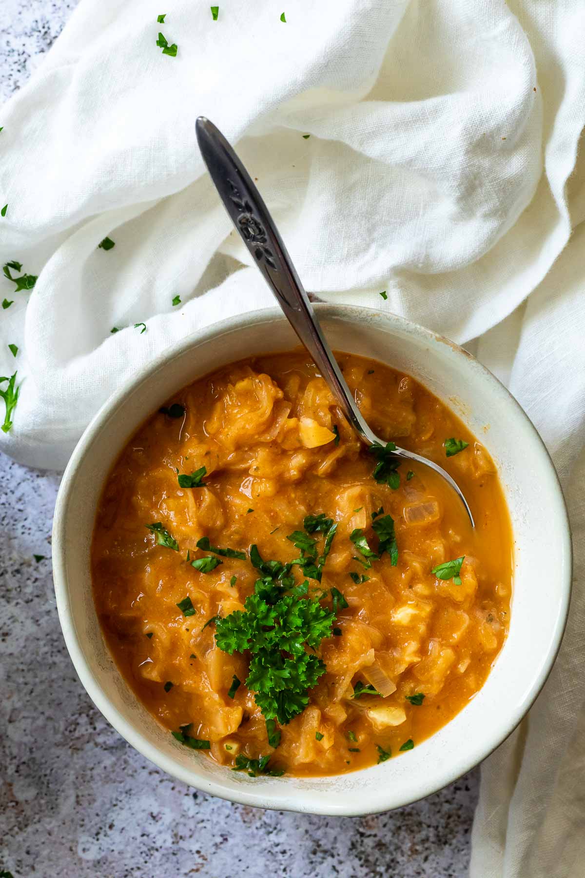 Eine Schüssel vegane Sauerkrautsuppe mit einem Löffel und einem Tuch daneben.