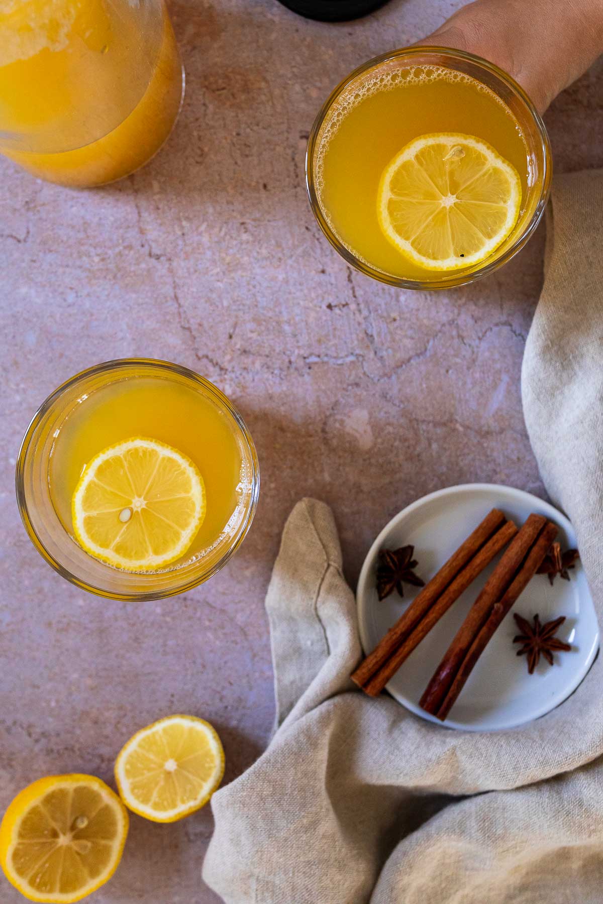 Bird view of two cups of warm winter lemonade with a mini plate with cinnamon sticks and anise stars.