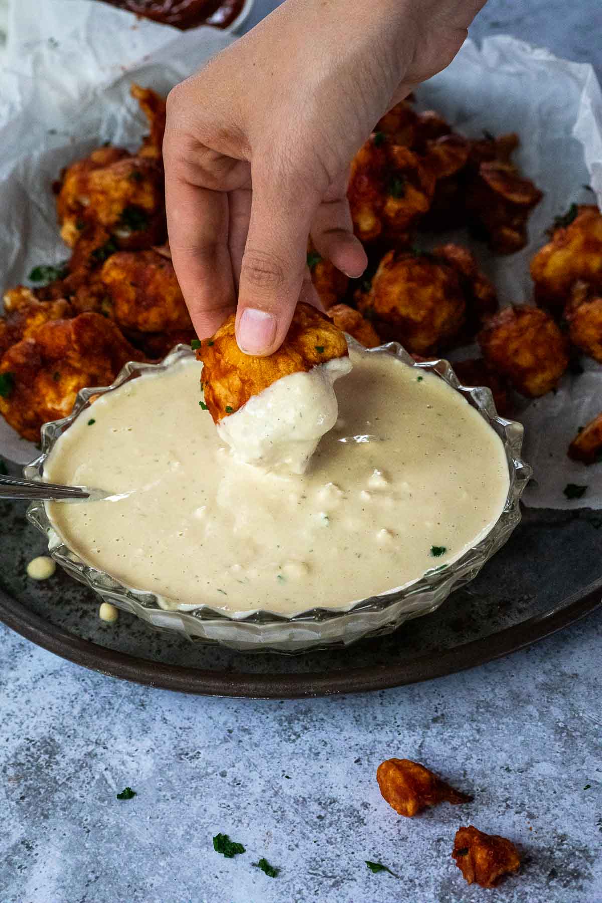 Tauchen Sie einen veganen BBQ Blumenkohlflügel in ein milchfreies Blauschimmelkäse-Dressing