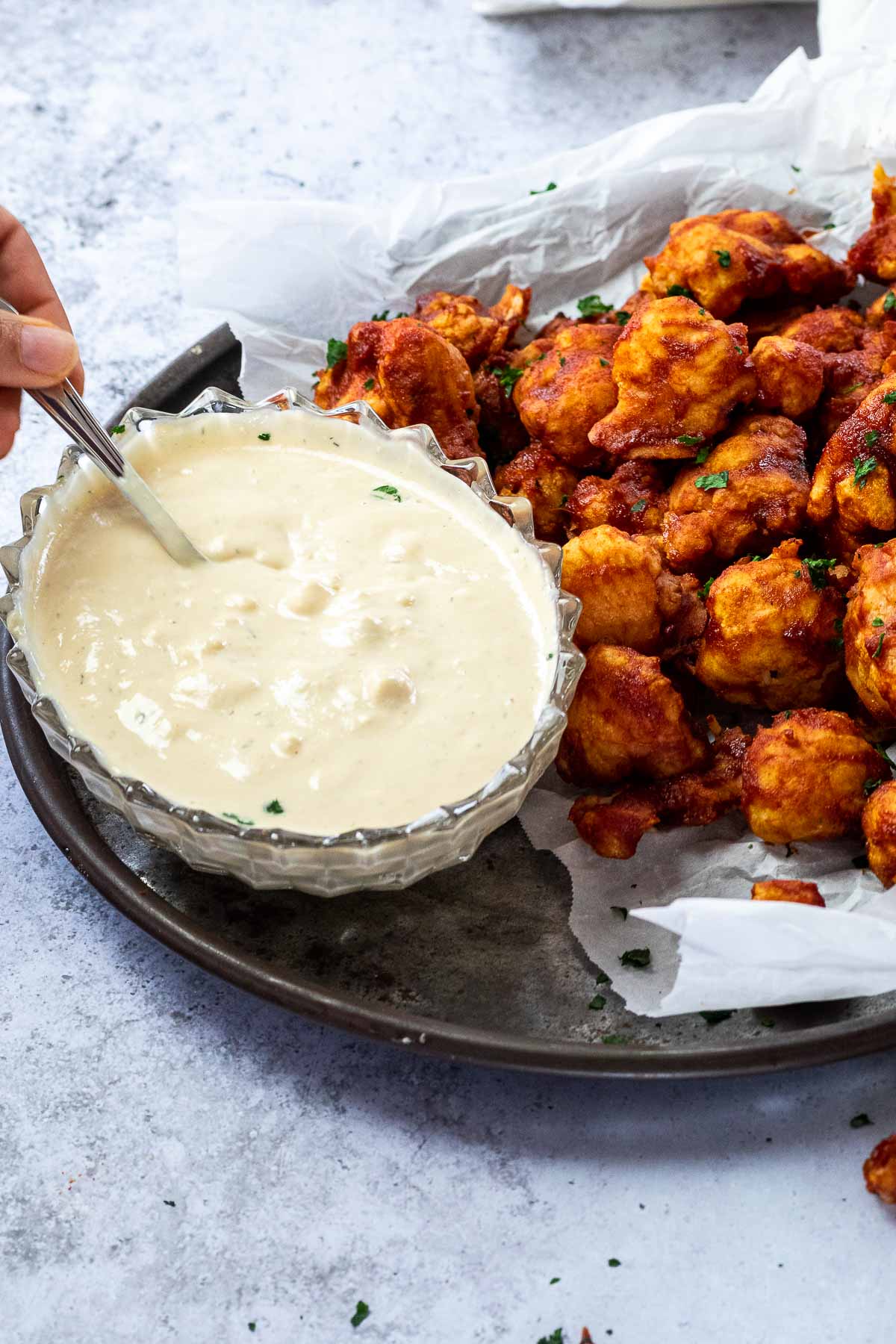 Bowl of vegan blue cheesedressing with a spoon served on a platter with bbq wings