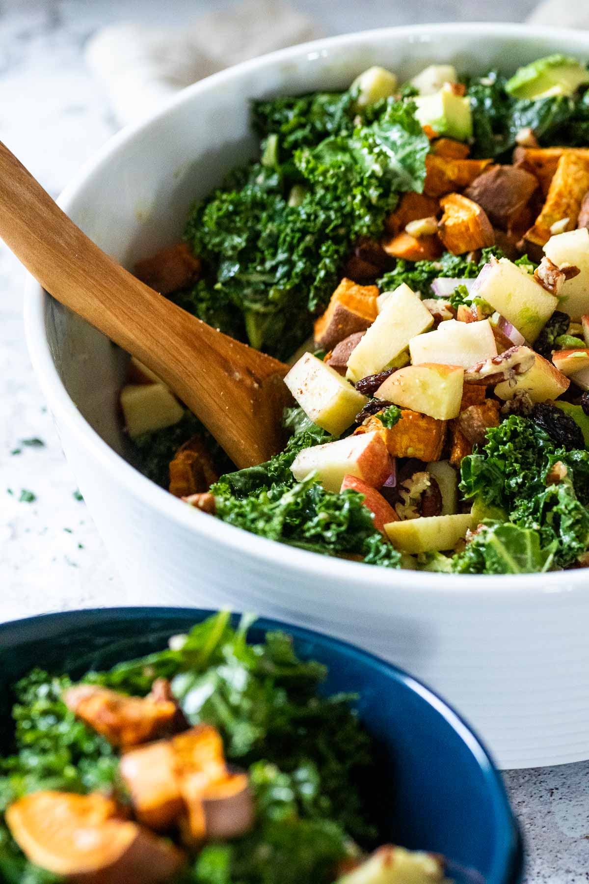 Im Fokus eine große Schüssel Grünkohlsalat mit einer verschwommenen blauen Schüssel vor