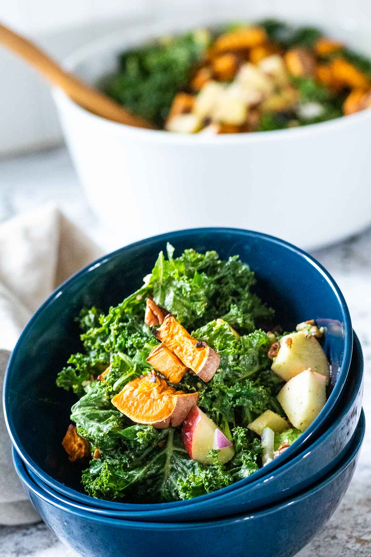 Staple of 3 blue bowls with kale salad on top with blurred big white bowl in the back