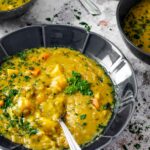 Eine Schüssel vegane Erbsensuppe mit Löffel im Fokus, zwei im Rücken verschwommen