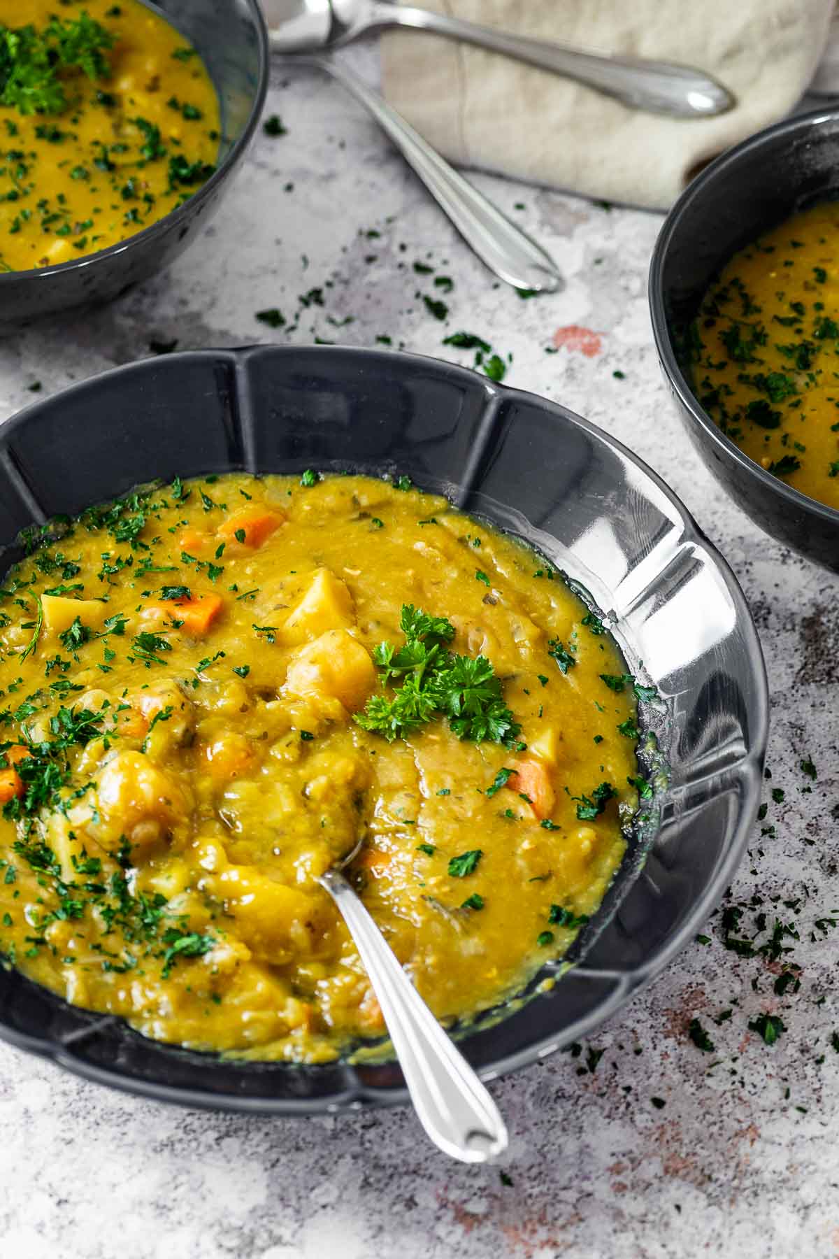 One bowl of vegan split pea soup with spoon in focus with two in the back blurred