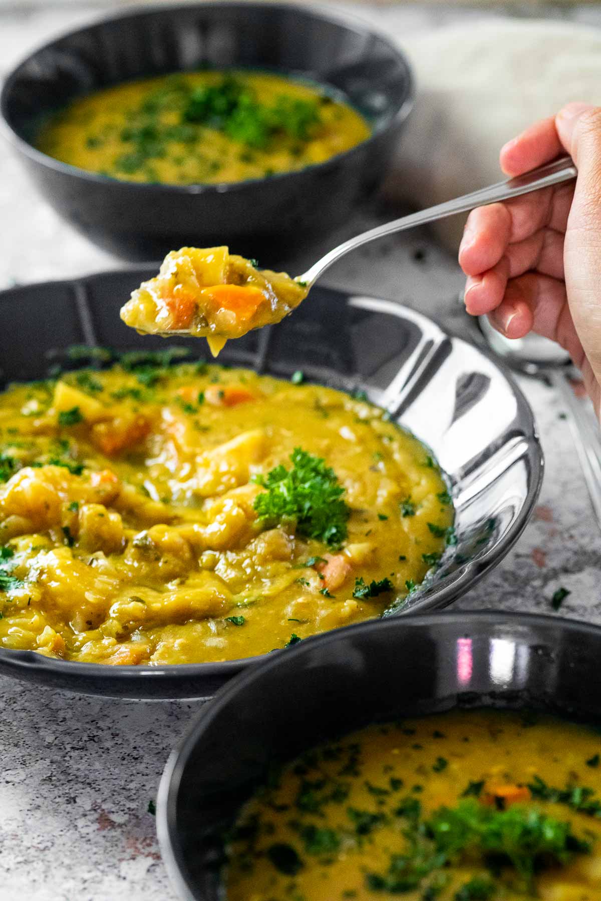 Vegan Split Pea soup on a spoon holding over a bowl of the soup