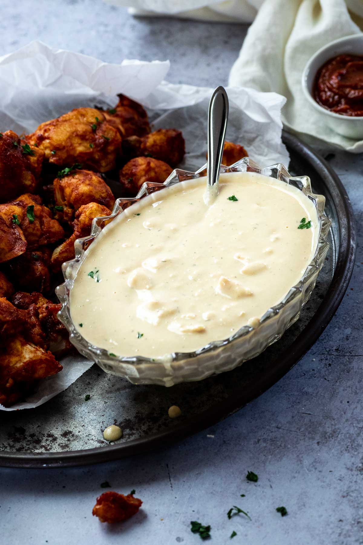 A bowl of vegan blue cheese dressing served on a platter with BBQ Cauliflower Wings