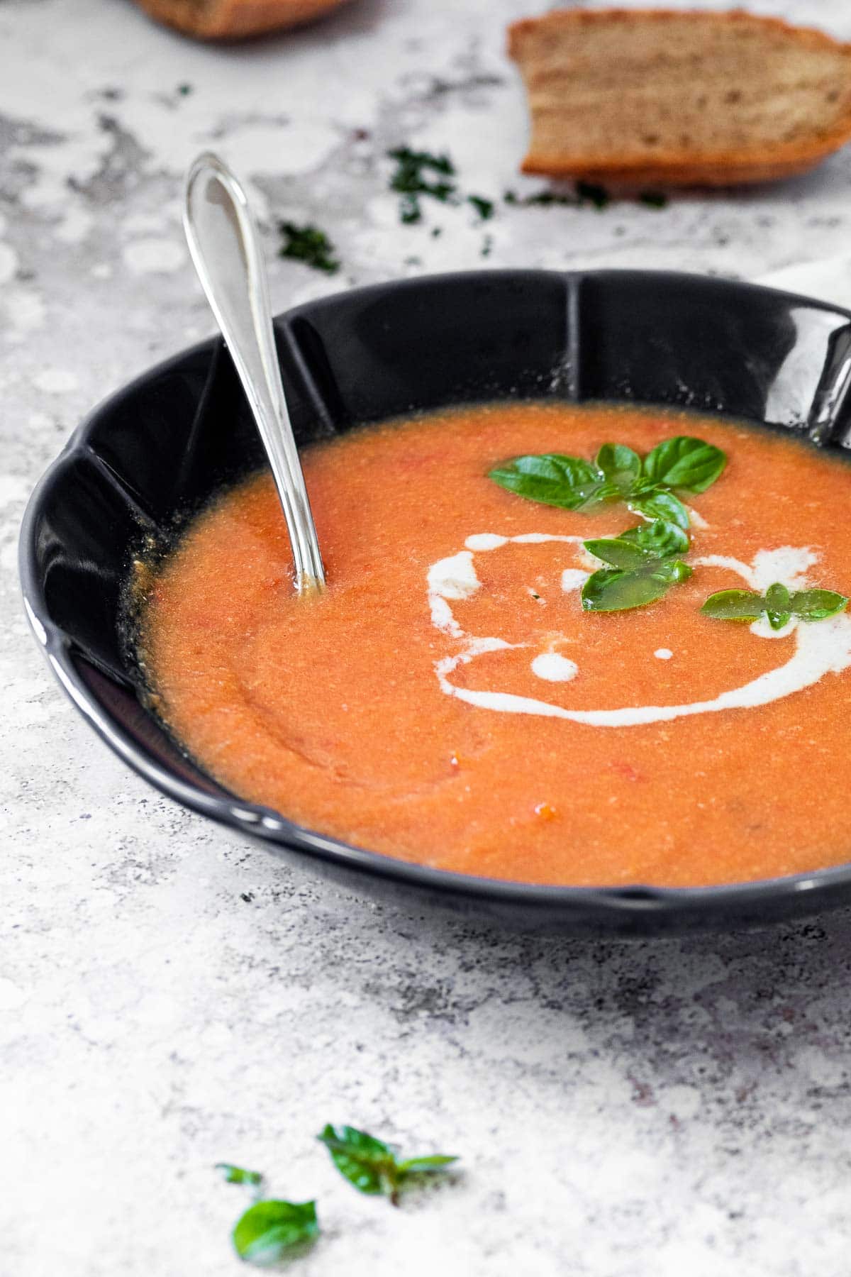 Schwarze Schüssel mit milchfreier Tomatensuppe und einem Löffel zum Essen.