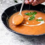 Halten Sie einen Löffel mit Tomatensuppe über die Schüssel.