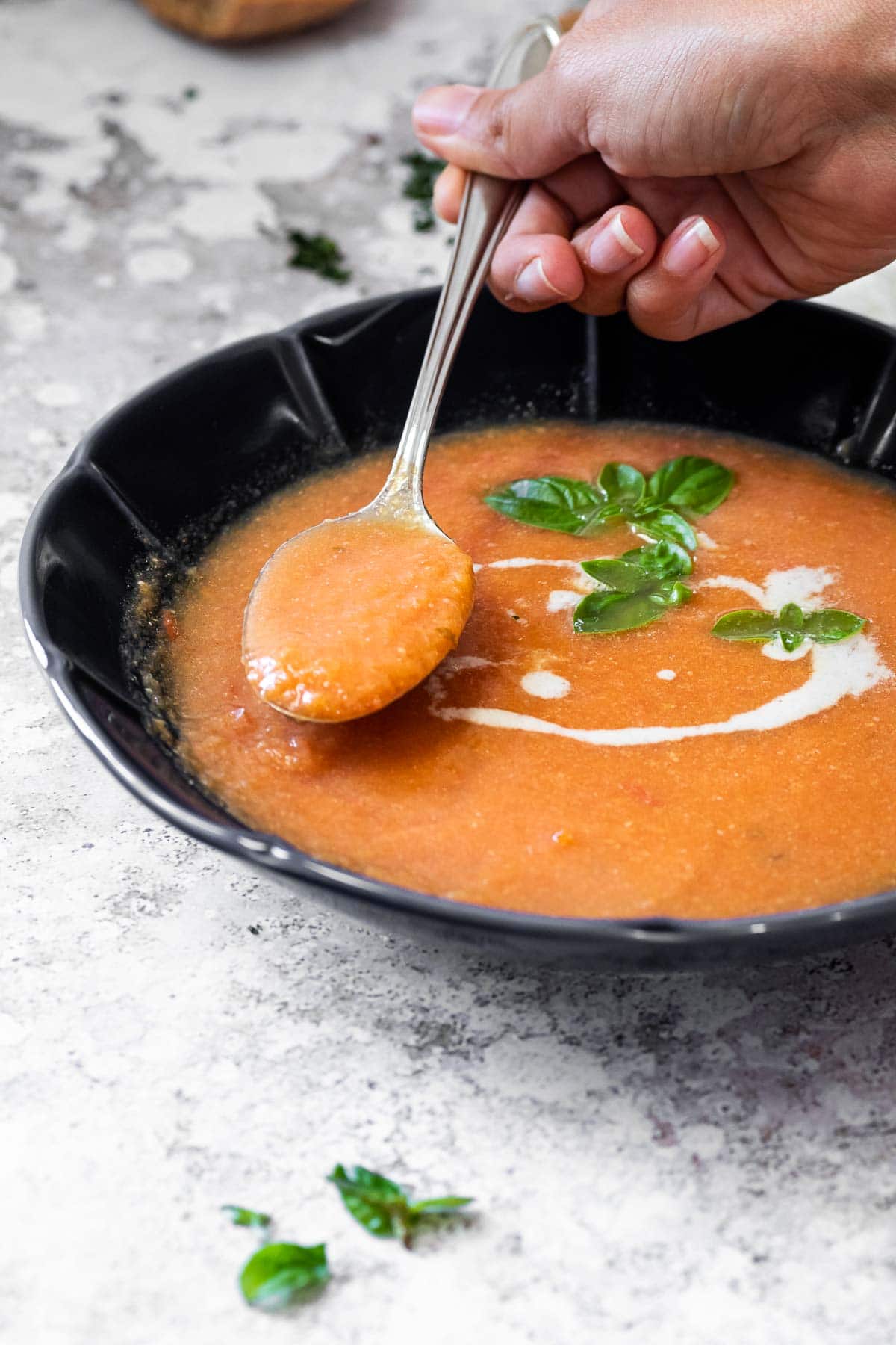 Holding a spoon with tomato soup over the bowl.