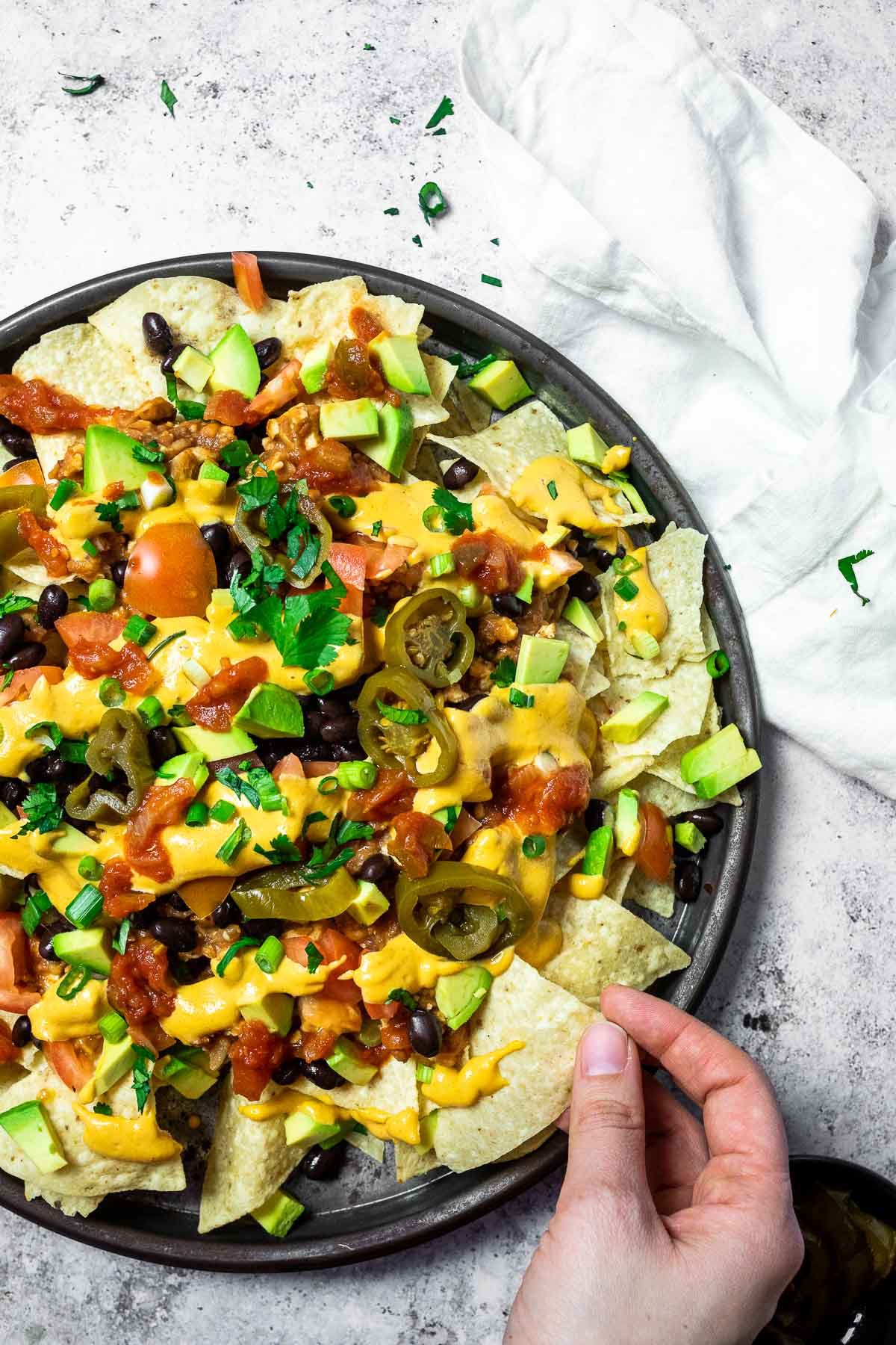 A hand is grabbing some nachos from the platter.