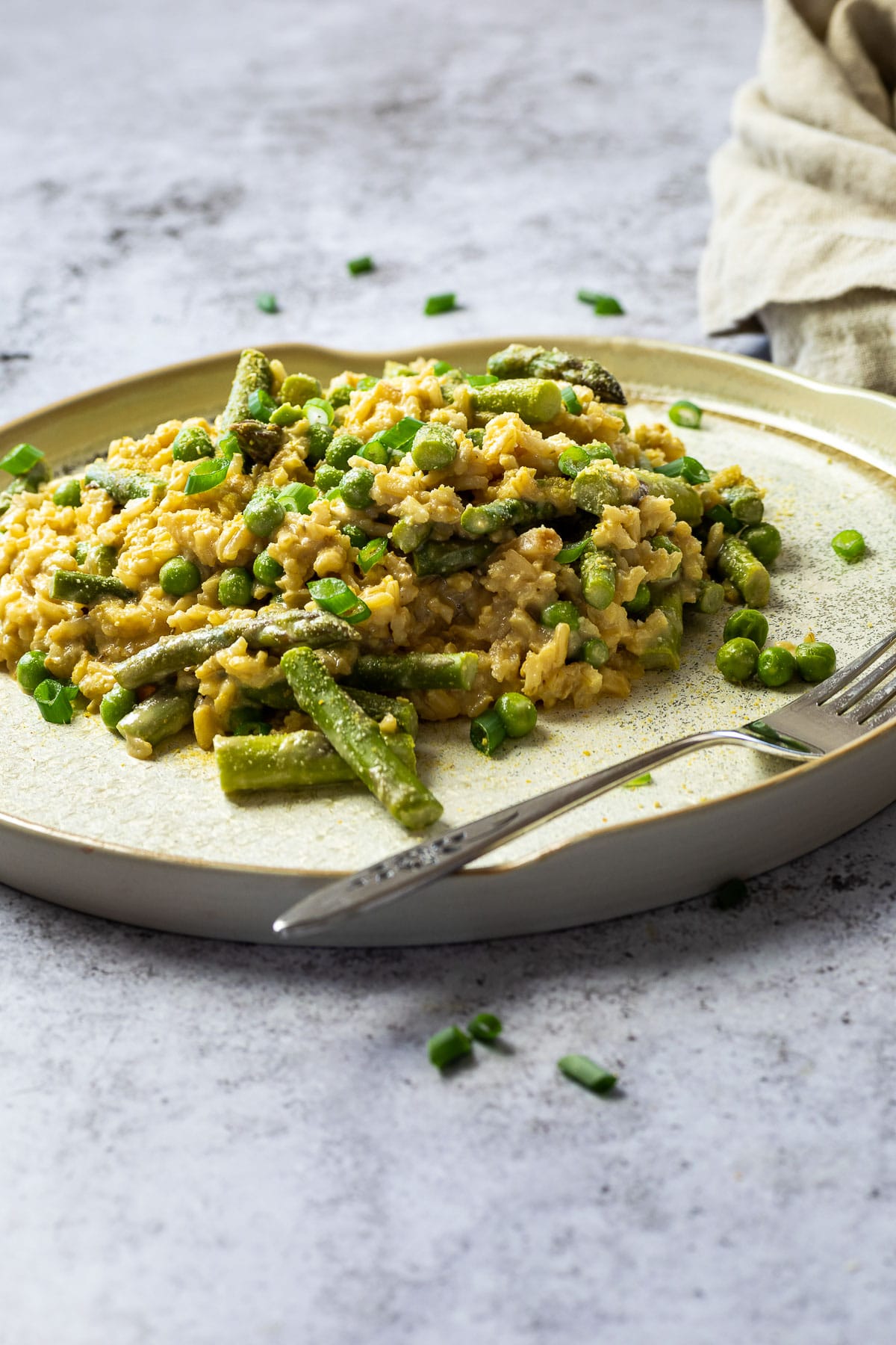 Ein anderer Winkel von pflanzlichem Erbsen- und Spargelrisotto mit einem Tuch im Hintergrund.