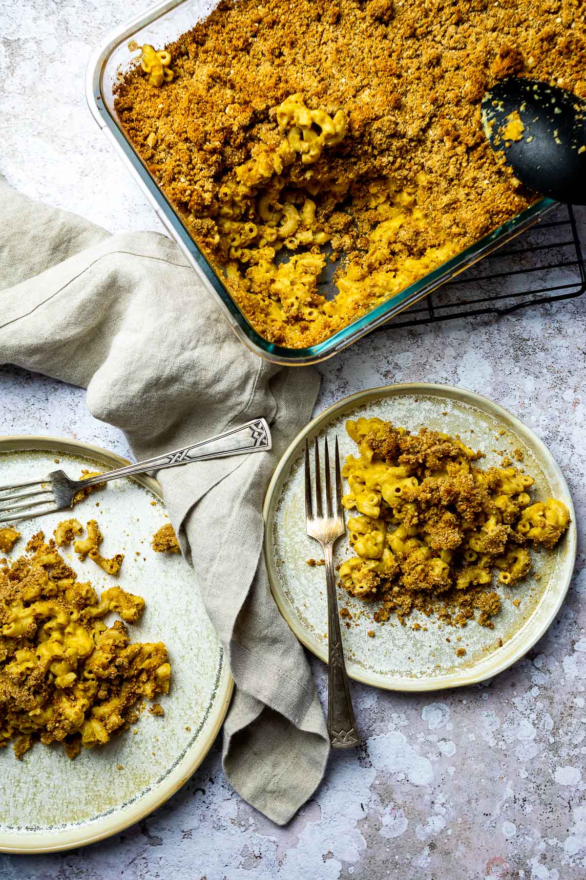 Vogelansicht eines gebackenen Mac-Käse-Auflaufs und zweier Teller mit vegan gebackenem Mac-Käse und zwei Gabeln.