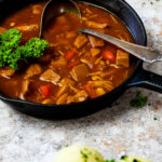 Meatless Hungarian Goulash in a cast iron pan with blurred potato dumplings in front.