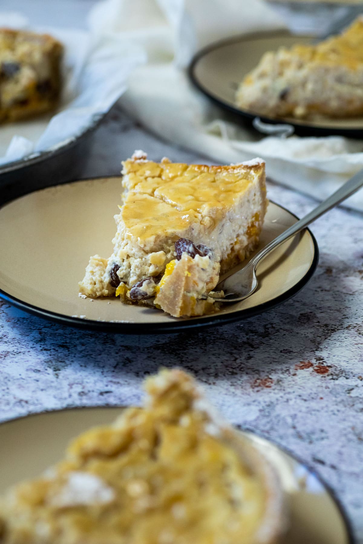 Piece of vegan Rice Pudding Pie on a plate in front of a pie pan and a plate. And in the back of a plate.