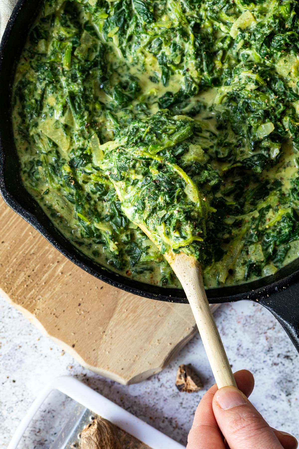 Holding a wooden spoon in the vegan creamed spinach.